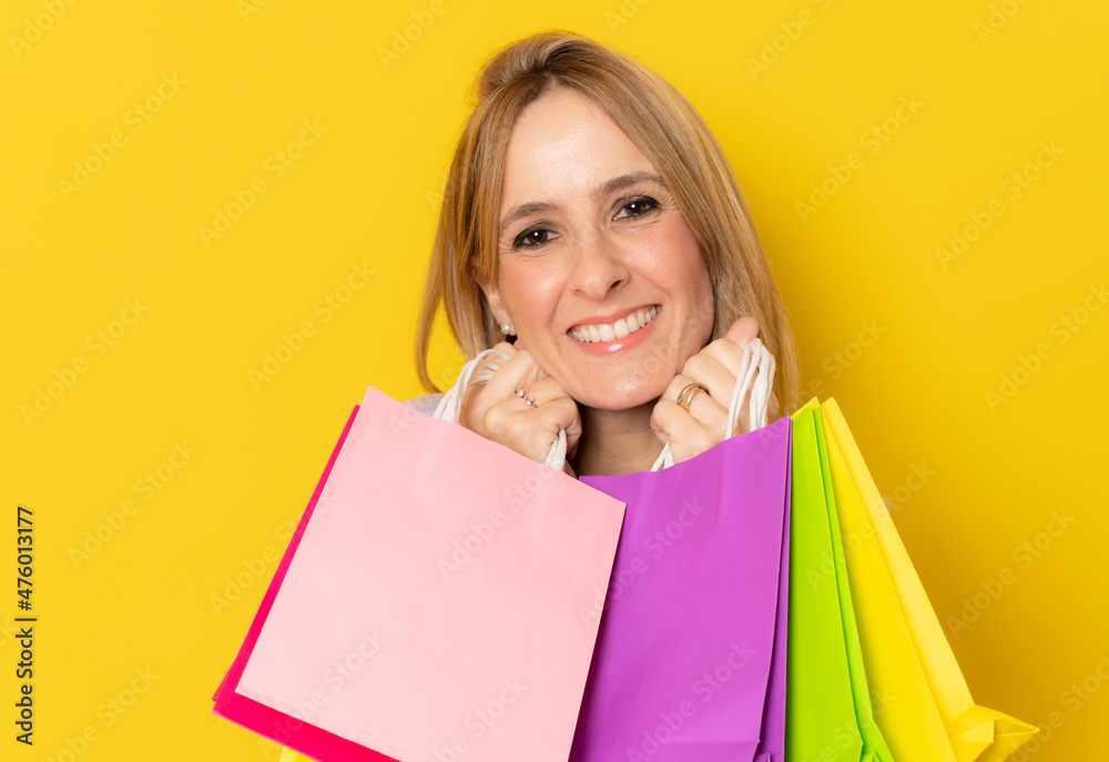 Close up portrait smiling woman with shopping bags isolated over yellow background.