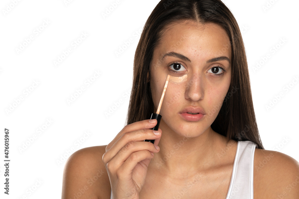 a young woman applies concealer under her eyes a young woman applies concealer under her eyes