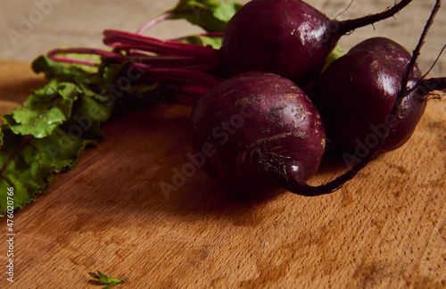 Close-up of a bunch of fresh burgundy beetroot with green tops and leaves on a wooden cutting board . Food background of seasonal raw vegetables