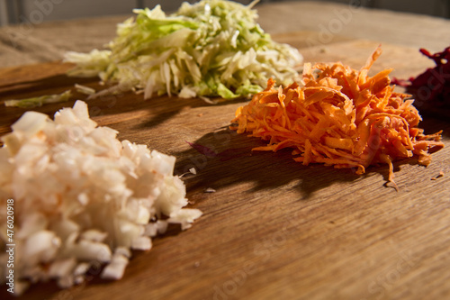 Chopped and grated raw fresh vegetables -beet, carrot onions and cabbage on a wooden cutting board. Close-up of chopped ingredients for a traditional Ukrainian soup- borscht