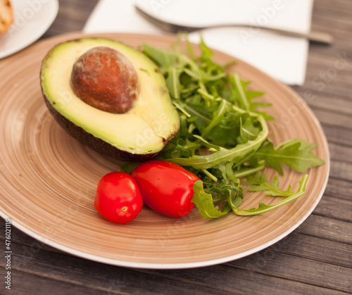 half an avocado, arugula and cherry tomatoes on plate