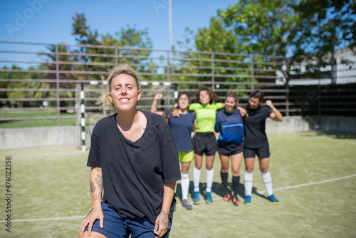 Portrait of young woman on football field. Sportswoman in dark uniform looking proudly at camera, teammates in background. Sport, leisure, female football concept