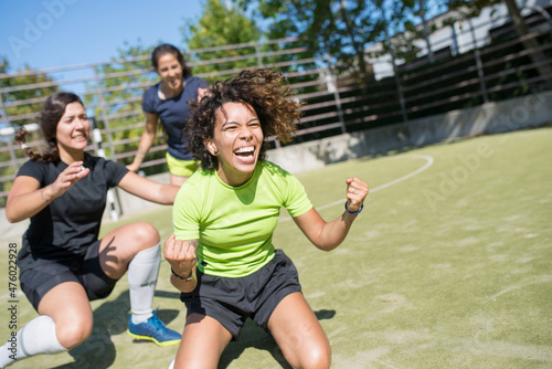 Overjoyed young women celebrating victory on football field. Sportswomen in uniforms cheering, congratulating teammate. Screaming happily. Sport, leisure, active lifestyle concept © KAMPUS