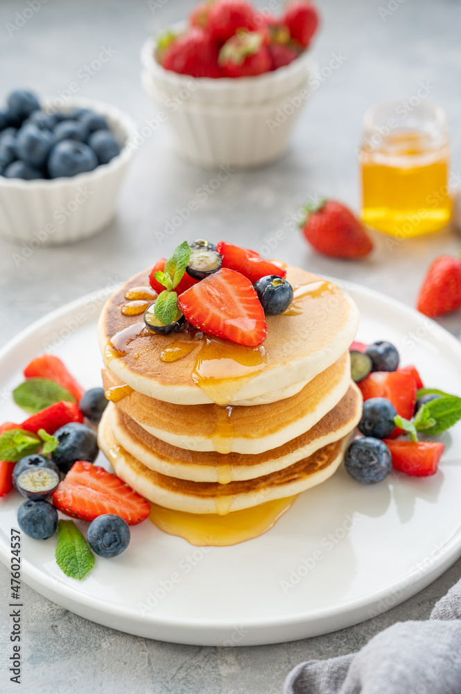 A stack of delicious fluffy pancakes with berries and honey on a white plate on a gray concrete background. Copy space. A stack of delicious fluffy pancakes with berries and honey on a white plate on a gray concrete background. Copy space.