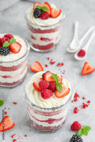 Red Velvet cake trifle with fresh berries in a glass jar on a gray concrete background. Dessert for Valentine s Day. Copy space.