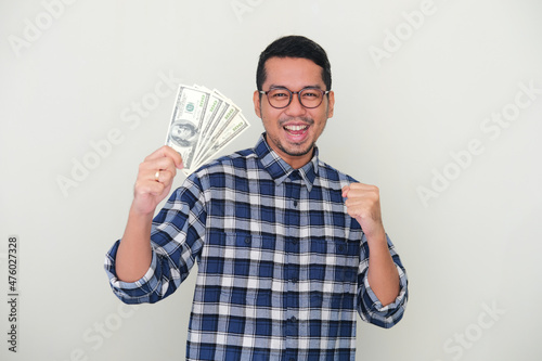 Adult Asian man clenched fist and showing happy expression while holding united states dollar paper money