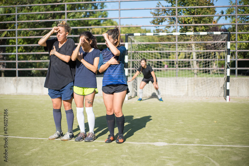 Young sporty women standing on football field. Sportswomen different uniforms standing before goals, shielding eyes from sun with hands. Sport, leisure, active lifestyle concept © KAMPUS