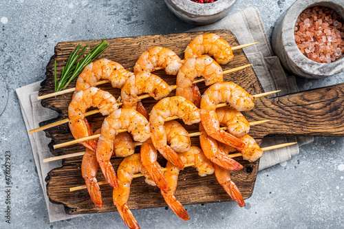 BBQ Roasted shrimps prawns on skewers on a wooden board with herbs. Gray background. Top view