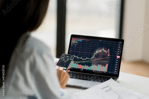 Successful smart woman crypto trader, an investor, using laptop and phone, analyzes the charts of trading in the stock market of digital cryptocurrency exchange, analyzes, buys and sells crypto coins