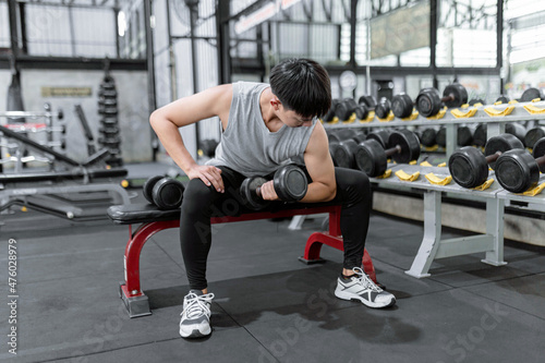 exercise concept The sport man picking up the dumbbell with his left hand while another dumbbell on the bench next to his right