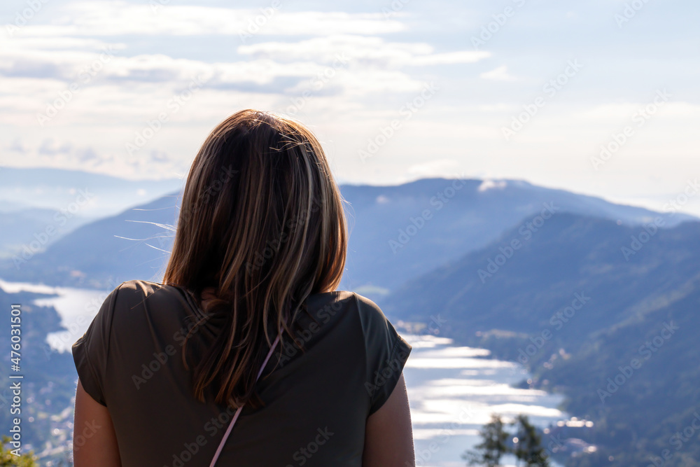 A woman standing at the viewing platform of a chapel at the top of Oswaldiberg with the view on the Lake Ossiach in Austrian Alps, Carinthia. The woman enjoys panoramic view. Morning vibe, Freedom A woman standing at the viewing platform of a chapel at the top of Oswaldiberg with the view on the Lake Ossiach in Austrian Alps, Carinthia. The woman enjoys panoramic view. Morning vibe, Freedom