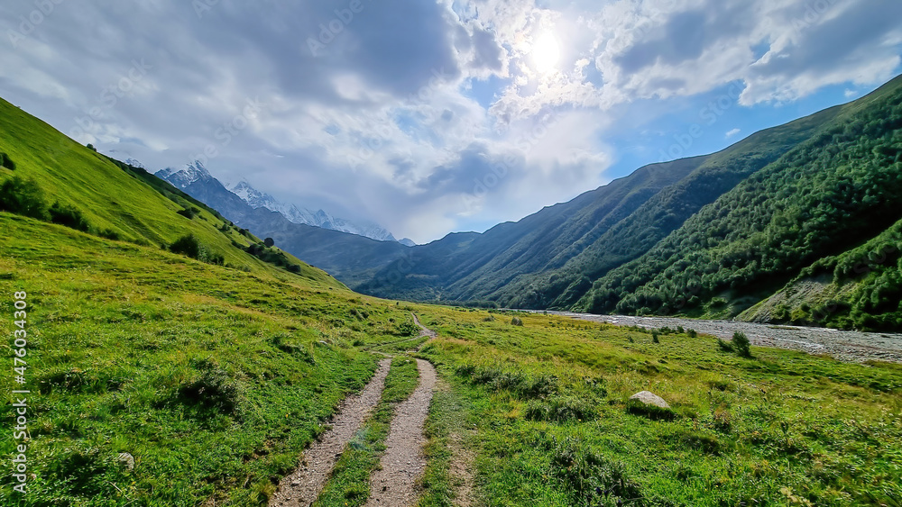 A hiking trail along the Adishischala river, located in Greater Caucasus Mountain Range in Georgia, Svaneti Region. The early morning sun beams are touching is touching the path. Wanderlust
