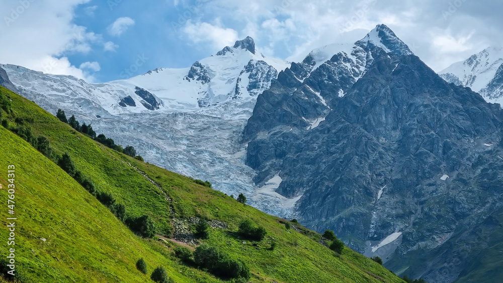 A panoramic view on the snow-capped peak of Jangi-Tau(Dzhangi-Tau) in the Greater Caucasus Mountain Range in Georgia, Svaneti Region. Hills with lush pastures, sharp peaks, hiking vibes.