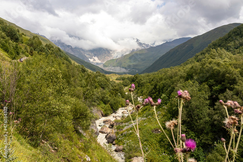 A panoramic view on the cloud covered peaks of Tetnuldi, Gistola and Lakutsia in the Greater Caucasus Mountain Range in Georgia, Svaneti Region. River Adishischala flowing down the valley.