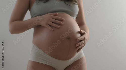 Pregnant woman smears belly with oil or cream from stretch marks standing indoors. Expectant mother takes care of her skin with cosmetics at home