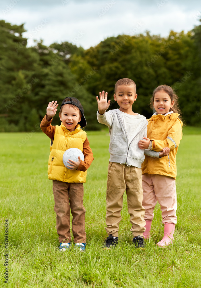 childhood, leisure and people concept - group of happy children with soccer ball waving hands at park childhood, leisure and people concept - group of happy children with soccer ball waving hands at park