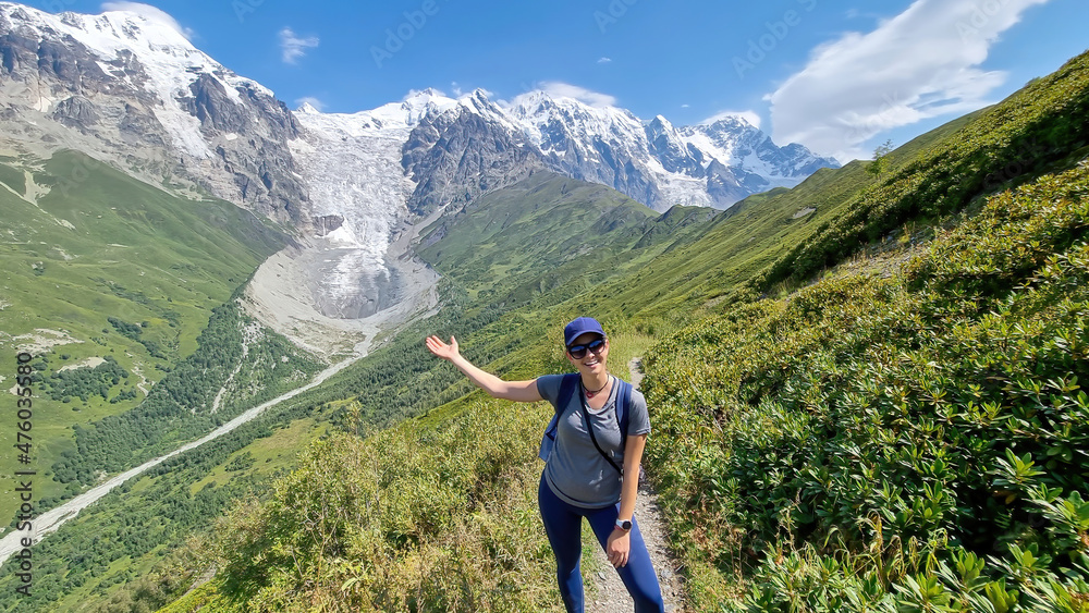 A woman on a hiking trail with a panoramic view on the snow-capped peaks of Tetnuldi, Gistola, Lakutsia and the Adishi Glacier in the Greater Caucasus Mountain Range in Georgia,Svaneti Region.