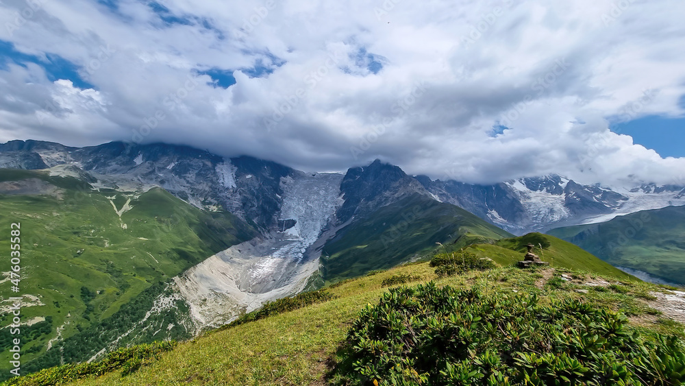 Fototapeta premium A panoramic view on the snow-capped peaks of Tetnuldi, Gistola, Lakutsia and the Adishi Glacier in the Greater Caucasus Mountain Range in Georgia, Svaneti Region. Sharp peaks, wanderlust, solitude.