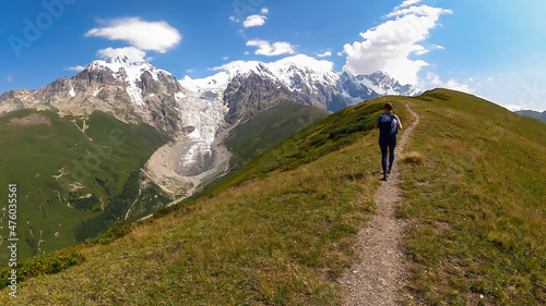 A woman on a hiking trail with a panoramic view on the snow-capped peaks of Tetnuldi,Gistola,Lakutsia and the Adishi Glacier in the Greater Caucasus Mountain Range in Georgia,Svaneti Region.Wanderlust