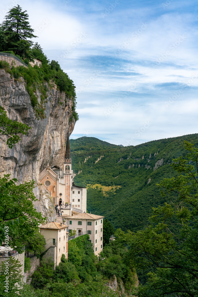 Monastery church perched on rocky cliff surrounded by forest, Madonna della Corona, Italy