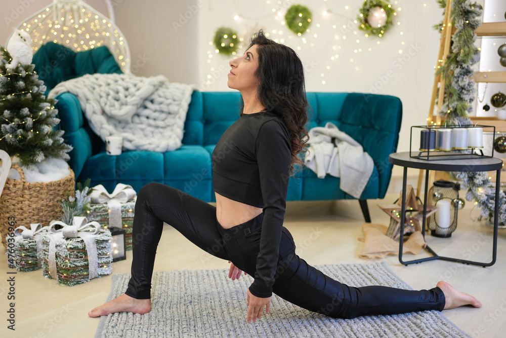 Obraz premium Middle age woman doing yoga near sofa and Christmas tree in home