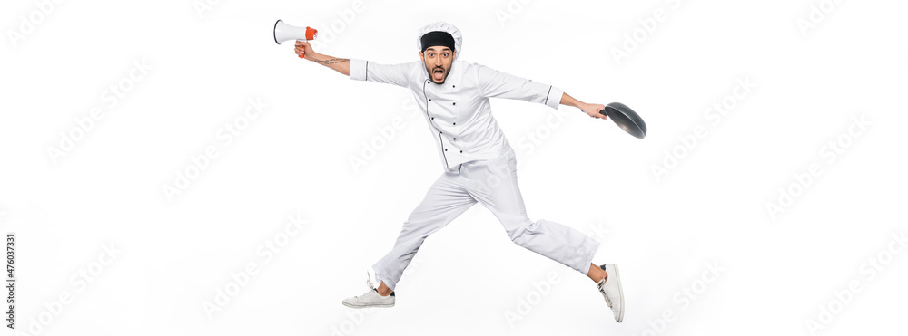 surprised chef in hat and uniform levitating while holding frying pan and megaphone isolated on white, banner.