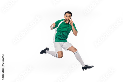 amazed football player in uniform jumping while talking on smartphone on white. © LIGHTFIELD STUDIOS