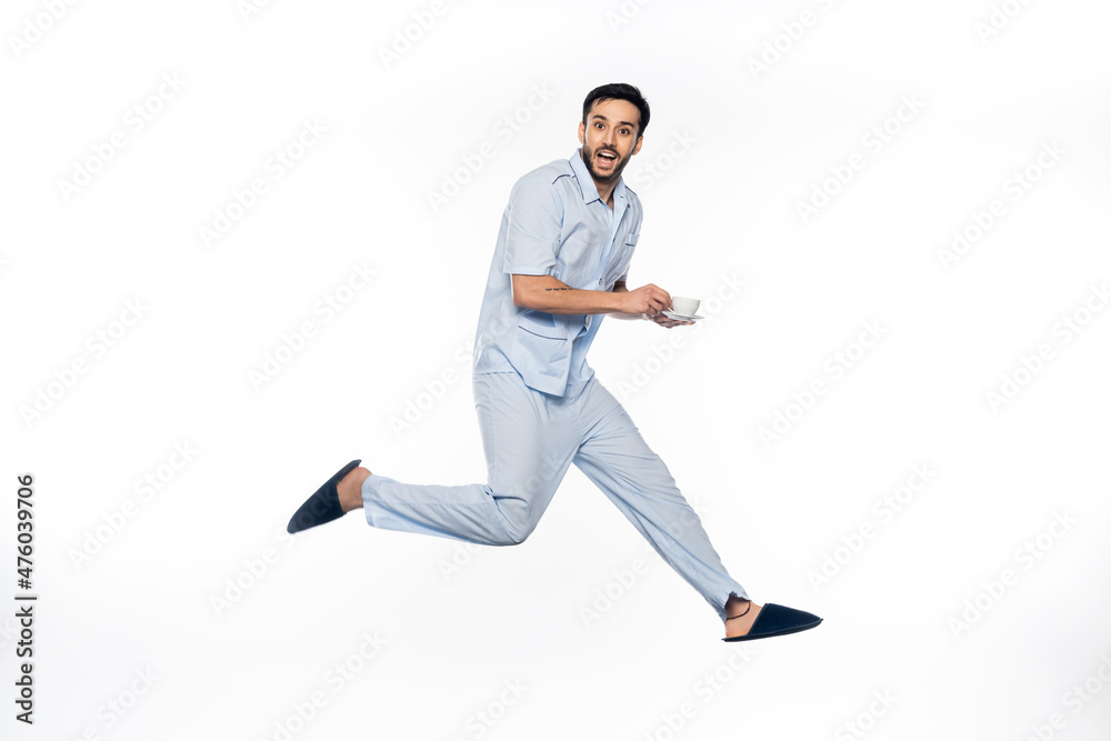 happy man in pajamas holding cup and saucer while levitating on white. happy man in pajamas holding cup and saucer while levitating on white.