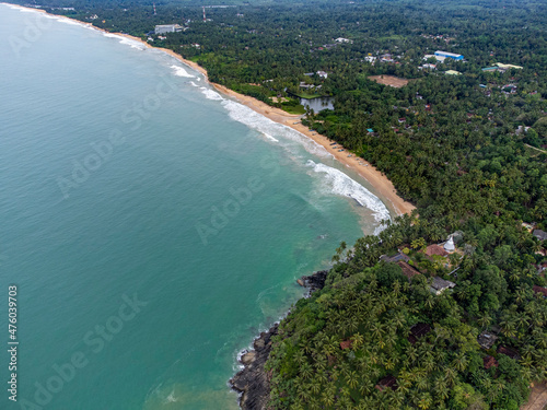 Sri Lanka. Ahungalla beach: ocean, coastal waves, sand. Tropical trees and palm trees grow along the beach line. Top view, shooting from a drone. © YURIY