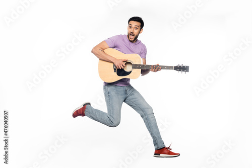 amazed man in jeans and purple t-shirt levitating while playing acoustic guitar on white.