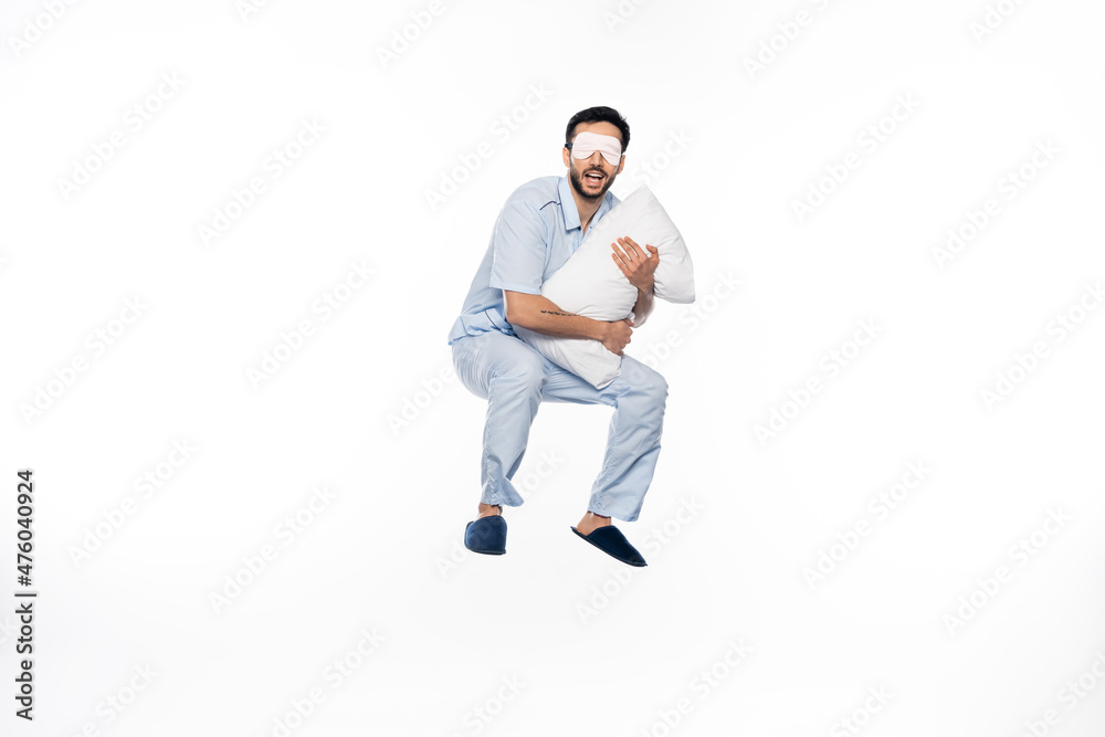 Naklejka premium happy man in pajamas and sleeping mask levitating with pillow on white.