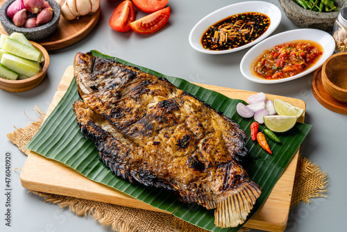 Gurame Bakar or Grilled Gourami with indonesian spices served on tray and banana leaf and isolated gray background. photo