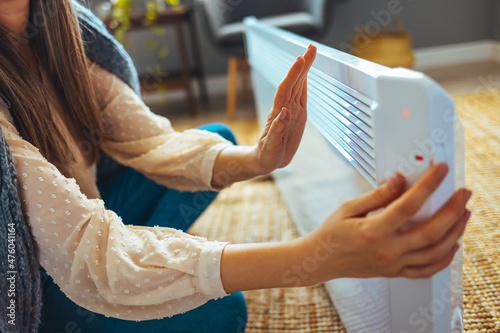 Woman warms up hands over heater. Concept of the need for good central heating. Using heater at home in winter. Woman regulating temperature on heater. Heating season.