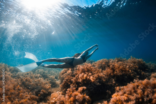 Free diver girl glides with freediving fins and sea bottom with seaweed. Freediving with woman and sunlight in blue ocean