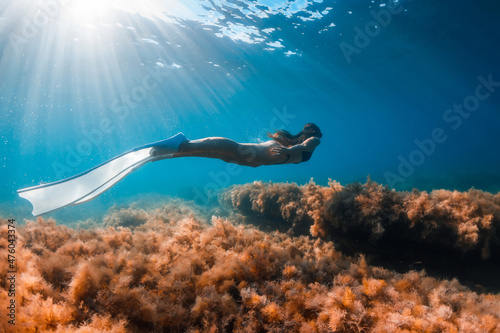 Free diver girl glides with freediving fins and sea bottom with seaweed. Freediving with woman and beautiful sun light in ocean