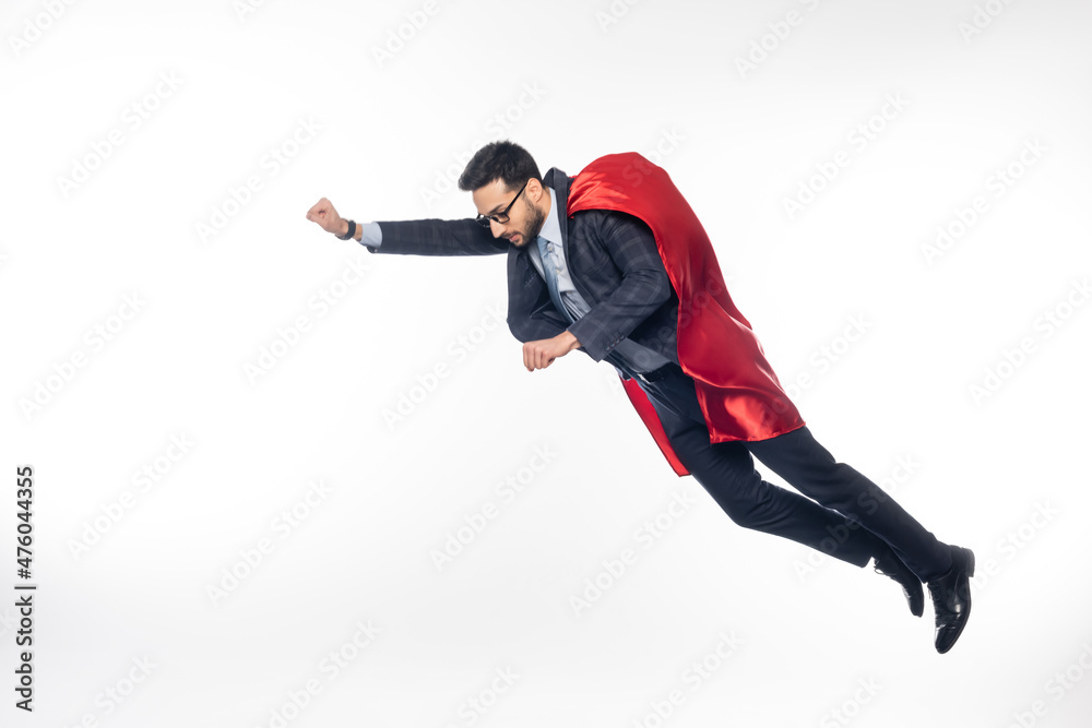 businessman in suit, glasses and superhero cape levitating on white.