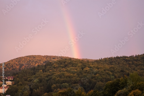 View of a colorful rainbow in the sky above a hill covered with dense deciduous forest. View of the mountainous areas and glades.