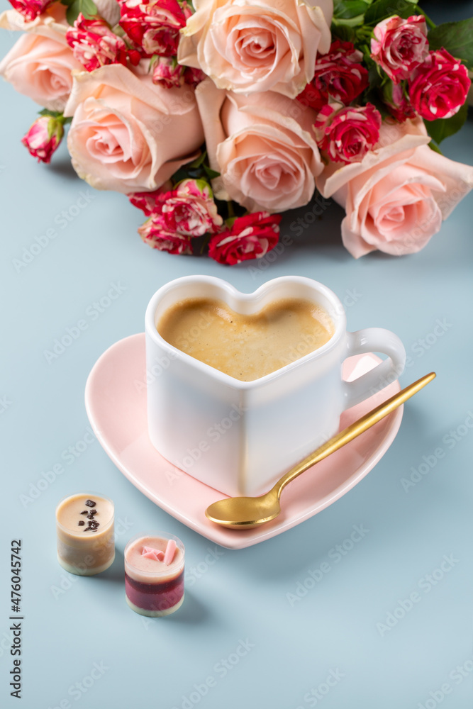 Cup of coffee in shape of heart with chocolate candies and bouquet of roses on blue background. Love concept. Cup of coffee in shape of heart with chocolate candies and bouquet of roses on blue background. Love concept.
