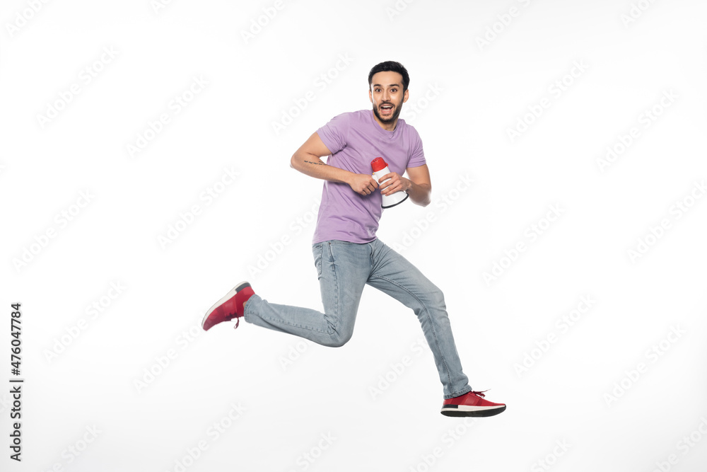 happy man in jeans and purple t-shirt levitating while holding megaphone on white.