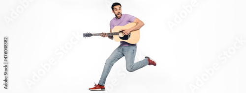 amazed man in jeans and purple t-shirt levitating while playing acoustic guitar on white, banner.