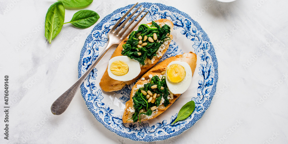 Fried spinach, egg and pine nuts sandwiches on light background. Delicious healthy breakfast or snack. Top view.