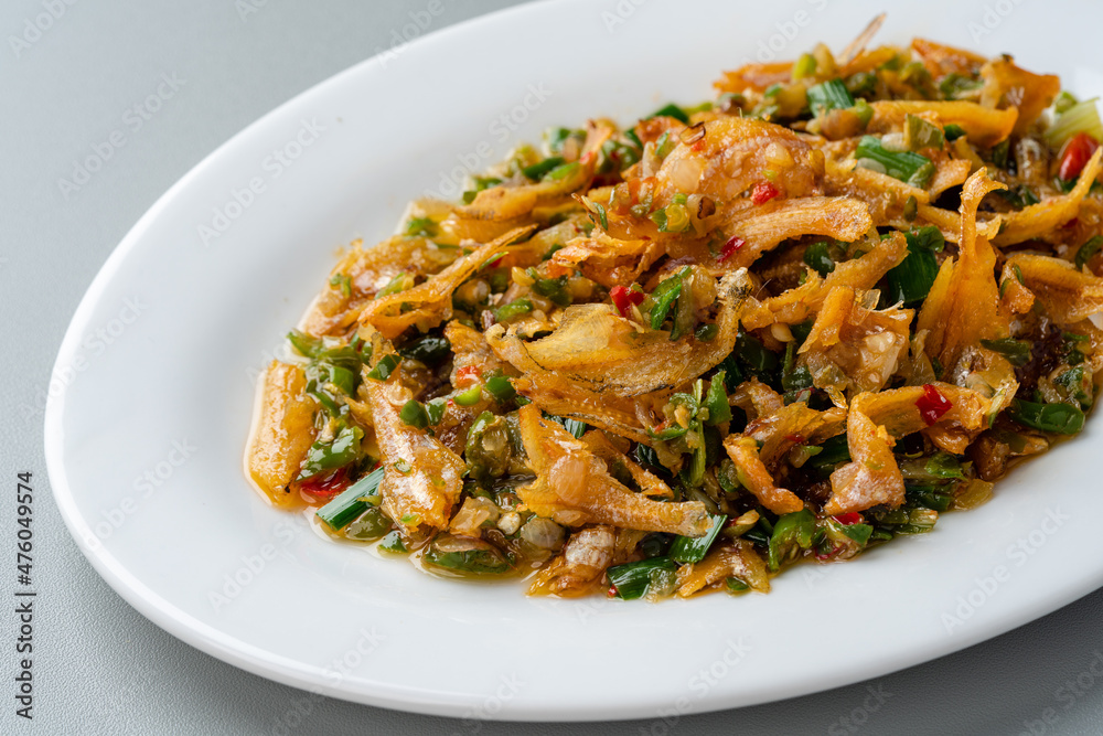 Fried anchovy cooked with green chili or ikan teri cabe ijo is a traditional food from west sumatra, Indonesia. served on white plate and isolated on gray background. Fried anchovy cooked with green chili or ikan teri cabe ijo is a traditional food from west sumatra, Indonesia. served on white plate and isolated on gray background.
