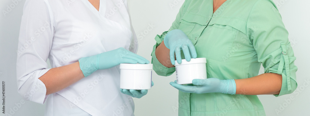 Two cosmeticians with jars of wax for depilation smiling against a white background. Natural product for hair removal. Copy space Two cosmeticians with jars of wax for depilation smiling against a white background. Natural product for hair removal. Copy space