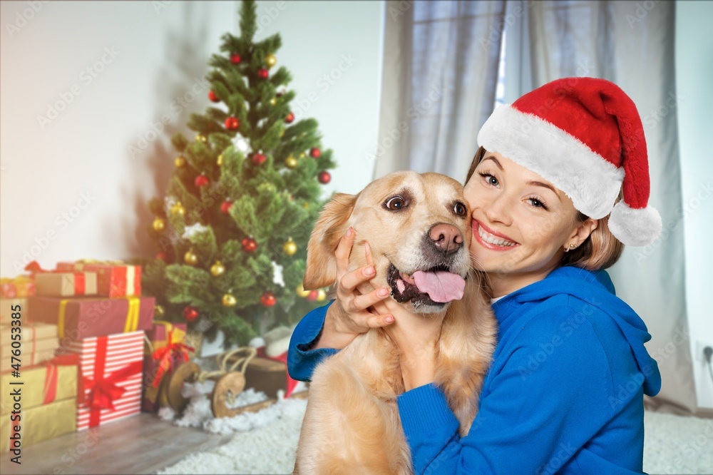 Happy girl in Santa hat, hugging dog with presents, on blurred background Happy girl in Santa hat, hugging dog with presents, on blurred background