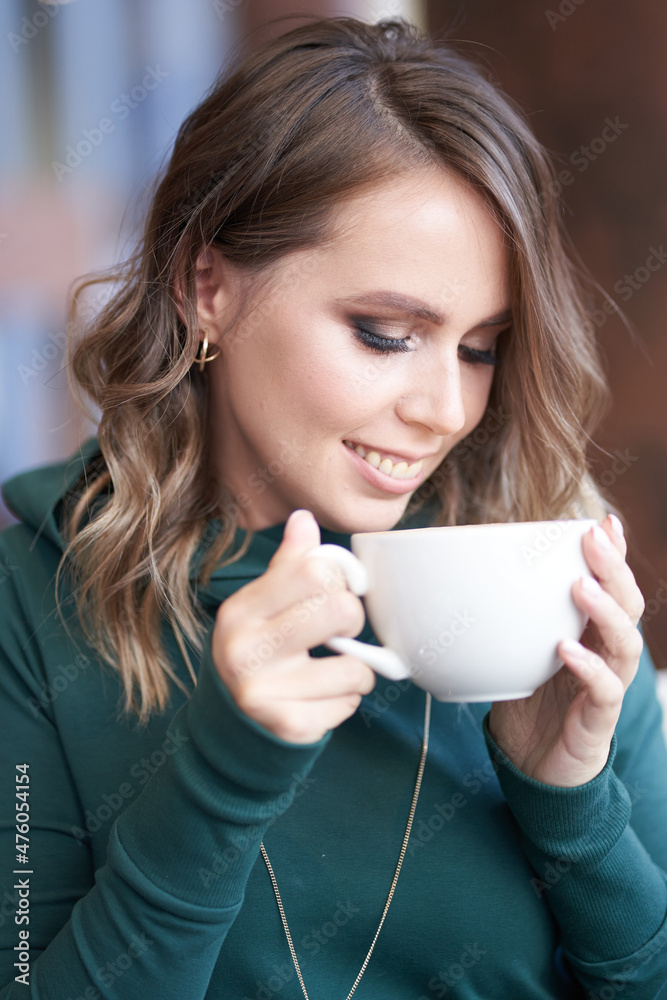 Photo of an optimistic beautiful brunette with a lady's hairstyle holding a cup of coffee, sitting in a cafe, a girl looks at a cup. High quality photo Photo of an optimistic beautiful brunette with a lady's hairstyle holding a cup of coffee, sitting in a cafe, a girl looks at a cup. High quality photo