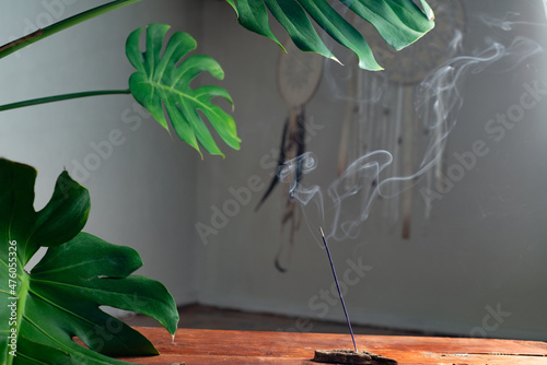 Smoke from an incense stick on the background of an interior with indoor plants and dream catchers. Meditation and mental health concept photo