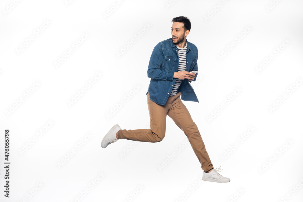 happy man levitating while holding smartphone and looking away on white.
