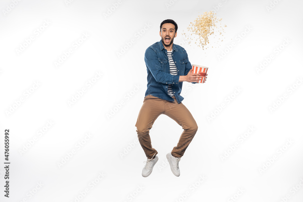 excited man levitating while holding bucket near flying popcorn on white. excited man levitating while holding bucket near flying popcorn on white.