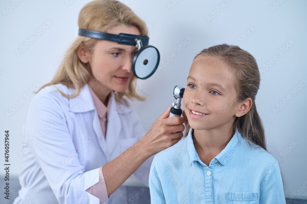 Woman examining girls ear through frontal reflector Woman examining girls ear through frontal reflector