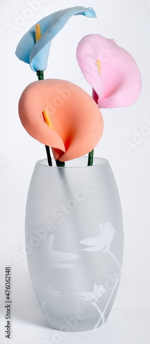 Three pastel colored foam lilies in a frosted white glass vase against a white background. photo